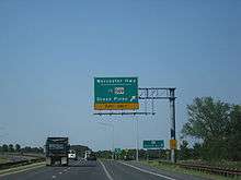 A divided highway curves to the left as the rightmost lane exits underneath an overhead green sign indicating the ramp leads to Worcester Highway and MD&nbsp;589 toward Ocean Pines.