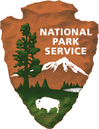 The National Park Service logo depicts an outline of a brown, jagged arrowhead, embedded in which are the silhouettes of a large green tree, a white mountaintop, and a grazing white bison. The words "National Park Service" hover above the mountaintop.