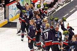 Several women wearing blue hockey jerseys wave to a crowd.