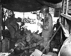 Medics treat a pair of injured men in a tent in the middle of a jungle