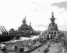 Two large battleships sailing toward the viewer. Personnel can be seen on the decks of both ships.