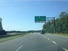 A four-lane asphalt road with a grassy median approaching an interchange. A green overhead sign reads MD 90 east Ocean City 1/4 mile west Salisbury exit only.