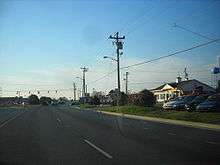 A divided highway approaching a signalized intersection with DE&nbsp;24, which is marked on a small sign to the right of the roadway