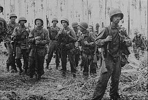 Soldiers with rifles slung standing in a jungle clearing