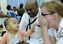 US Navy 100406-N-7478G-346 Operations Specialist 2nd Class Reginald Harlmon and Electronics Technician 3rd Class Maura Schulze play peek-a-boo with a child in the Children's Ward at Hospital Likas