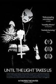 film title, awards and critical commentary imposed over a stark black-and-white image of a man in black metal-wear – black clothing, spikes and corpse paint – holding an inverted cross