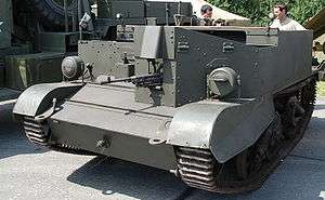 Colour photo of an open-topped armoured and tracked vehicle, painted dark green