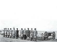 Eleven armed women at attention next to a cannon