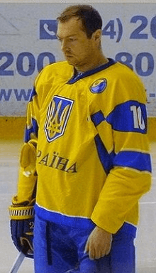An ice hockey player with his helmet and gloves off standing on the ice looking down