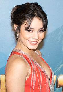 A woman with long dark hair wearing a red dress smiles and looks to the camera.