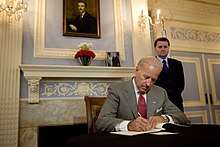 Joe Biden sits at a desk, writing in a book