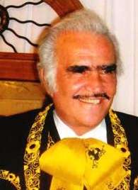 An aged man smiling wearing a charro suit.