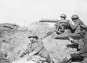 Four men in a barren landscape with a tripod-mounted machine gun