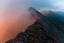 a series of jagged mountain peaks with a pinkish fog rising on the left side