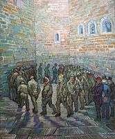 In an indoor prison yard a large group of men walk in a circle, one behind the other. The face of the prisoner in the centre of the painting and looking toward the viewer looks like Van Gogh.
