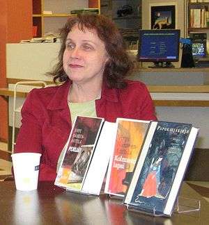 Woman in a red jacket sitting at a table, on which three of her books are displayed