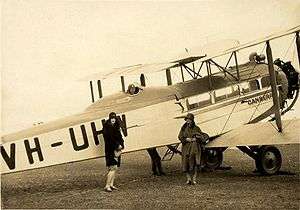 Two women standing in front of large biplane with man in flying gear seated in open cockpit
