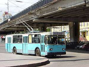 Aquamarine-and-white trolleybus under a viaduct