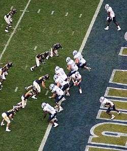 Several American football players in white and navy uniforms in action at the end zone area of the field.