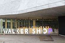 Window of a modern store, large lighted letters spelling Walker Shop in white, with the P in purple