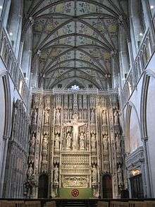 The photo shows the altar of St. Alban's Cathedral, behind which rises a large stone screen with tiers of statues, and a crucifix, centrally placed.