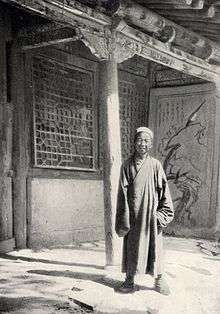 A black-and-white picture of an elderly Chinese man in front of a building