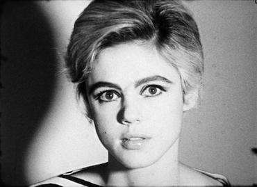 Black-and-white image of a woman with short light hair shown from the neck up against a light background. Her head fills the center of the image from top to bottom and casts a shadow on the background to her right.