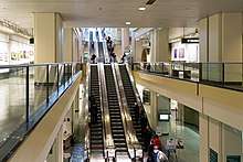 A bank of three escalators inside a hallway, with large columns and glass barriers