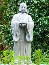 Sculpture of a monk with East Asian traits, holding an alms bowl.