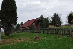 A wooden barn atop a lush green hill, with a wooden picket fence running through the center of the image.