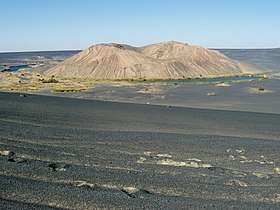 A white hill within a black depression, with lakes and vegetation at its foot and desert elsewhere
