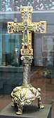 A golden cross on a pedestal, highly decorated, showing Jesus on the cross