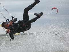  Kitesurfer wearing one-piece wetsuit, hanging from harness, separated from board.
