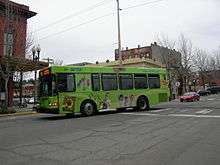 A green city bus pulls up to a stop