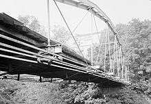 A black-and-white image of the bridge from the side and below, with a sign visible on top saying trucks and buses are not allowed across