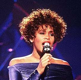 With brown hair, a woman holds a microphone wearing a purple garment.