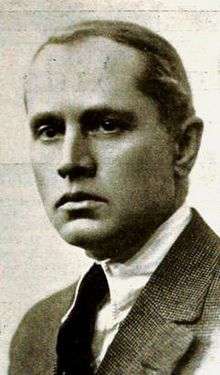 Black and white portrait photo of a white male wearing a jacket and tie.