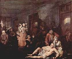A 1735 oil version of the last scene from William Hogarth's A Rake's Progress, the story of a rich merchant's son, Tom Rakewell whose immoral living causes him to end up in Bethlem. A shaven-head and near-naked Rakewell is depicted in one of galleries of Bethlem. He sits on the floor while his right leg is being manacled by an attendant. A wigged doctor is standing over him.  Rakewell's spurned fiancé kneels beside him, crying. Inmates exhibiting various stereotypical forms of madness are shown in their open cells and in the corridor. Two fashionably dressed lady-visitors standing by the cell of a "urinating mad monarch", are clearly amused by the show. One holds a fan up to her face and is clearly smiling while her companion whispers in ear. Hogarth became a governor of Bethlem in 1752.