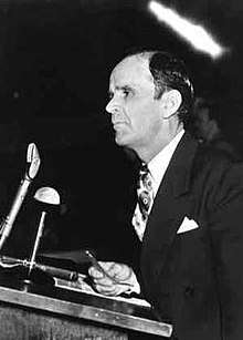 A man stands at a podium with a light colored object above his head