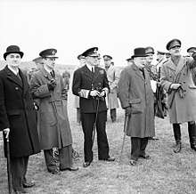 Churchill is surrounded by men in uniform. Lord Cherwell wears a bowler hat.