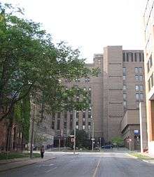 An image of the road leading up to a large, multi-story brick building. A tree is in front.