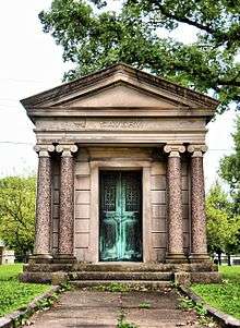 Stone mausoleum with four Ionic columns, an oxidized copper or bronze door and sign SAVERY above.