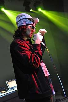 Photograph of a man in a red jacket holding a microphone.