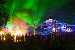 Festival attendees stand silhouetted against a multicoloured laser-light show