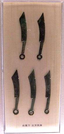 Five elongated bronze knives, corroded over time with a green color, with a ring handle on the end opposite the blade