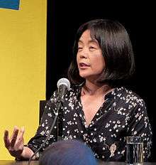 Yoko Tawada, seated, in front of a microphone