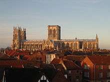 York Minster seen from the side - a long building with a pair of towers at one end and a massive central tower with two perpendicular windows. The round rose window can be seen on the south transcept.