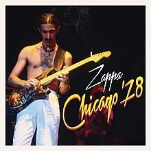 Frank Zappa onstage playing an electric guitar, wearing white pants and no shirt