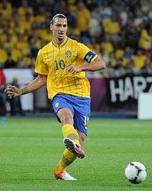 Zlatan Ibrahimović wearing a yellow shirt and blue shorts, passing the ball