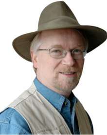 A headshot of Dr. Shawn Carlson smiling while wearing a hat